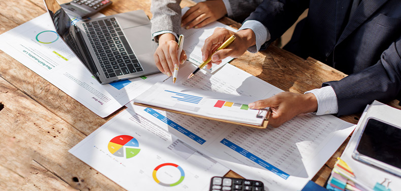 Close-up of business professionals reviewing charts and performance data on paper and laptop, symbolizing strategic planning and operational systems for scalable growth.